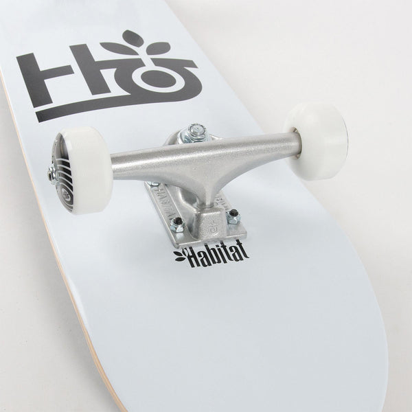 Close-up of a Habitat Pod Complete White skateboard deck and trucks with the brand logos visible.