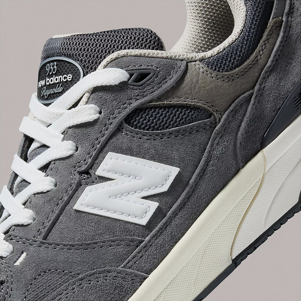 Close-up of the NB NUMERIC "GREY DAYS" REYNOLDS 933 sneaker in dark grey/white, highlighting suede and mesh textures, white laces, signature NB branding on the side and tongue, and a comfort-focused midsole—a standout heritage-inspired style.