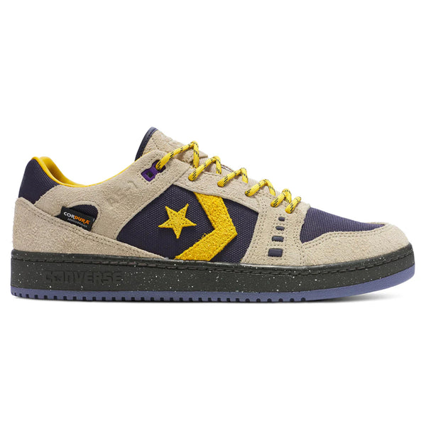 Introducing the CONVERSE CONS Alexis AS-1 Pro Cordura™ in Beach Stone and Baritone Blue: This low-top sneaker features a beige suede upper, highlighted with yellow and navy accents. It showcases a signature star logo and patterned laces, along with a dark sole featuring "Converse" branding. The design draws inspiration from Alexis Sablone for the CONVERSE CONS collection.