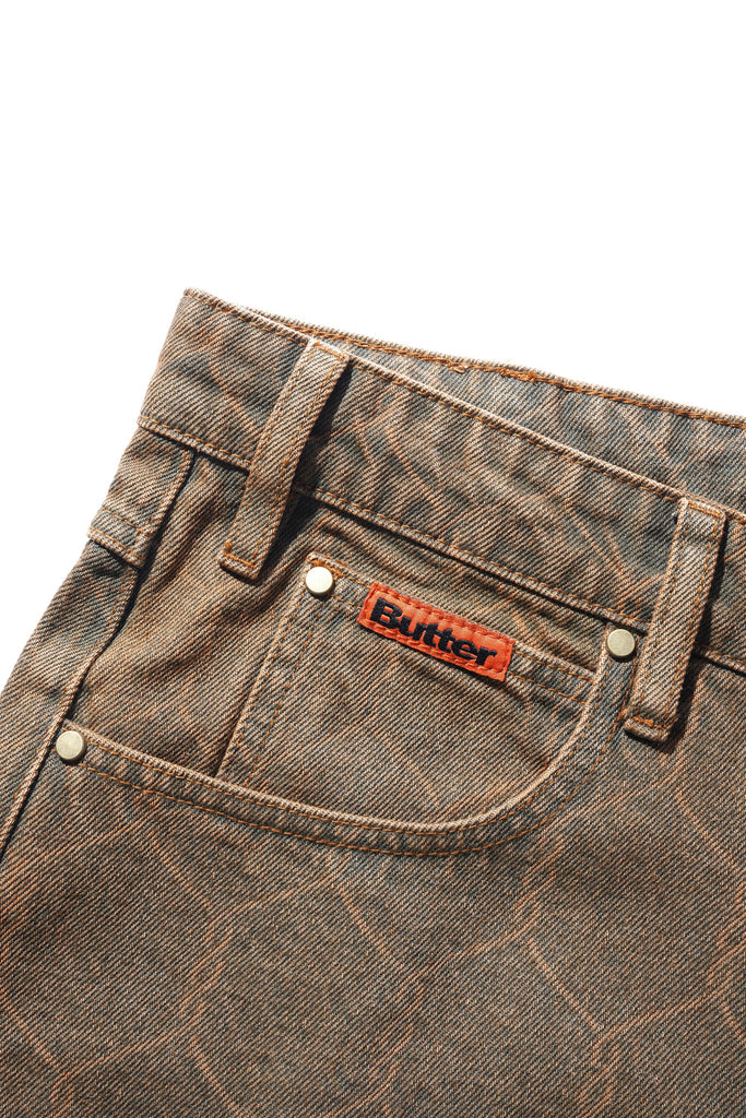 A pair of BUTTER GOODS CHAIN LINK DENIM JEANS WASHED BROWN pants with an orange logo.