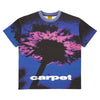 Introducing the Carpet Dandelion Tee Blue by Carpet Co.: a blue shirt featuring a striking graphic of a dandelion in pink and blue tones, screen printed to perfection. This unique design includes the word "carpet" subtly at the bottom, adding an artistic touch to your wardrobe.