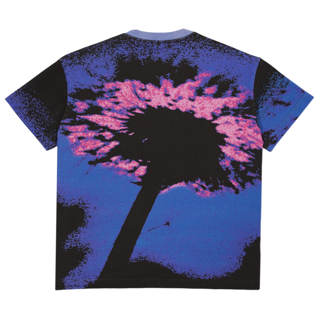 The Carpet Co. Carpet Dandelion Tee Blue showcases a palm tree silhouette set against a vivid blue and pink sky, screen printed on a comfortable blue shirt.