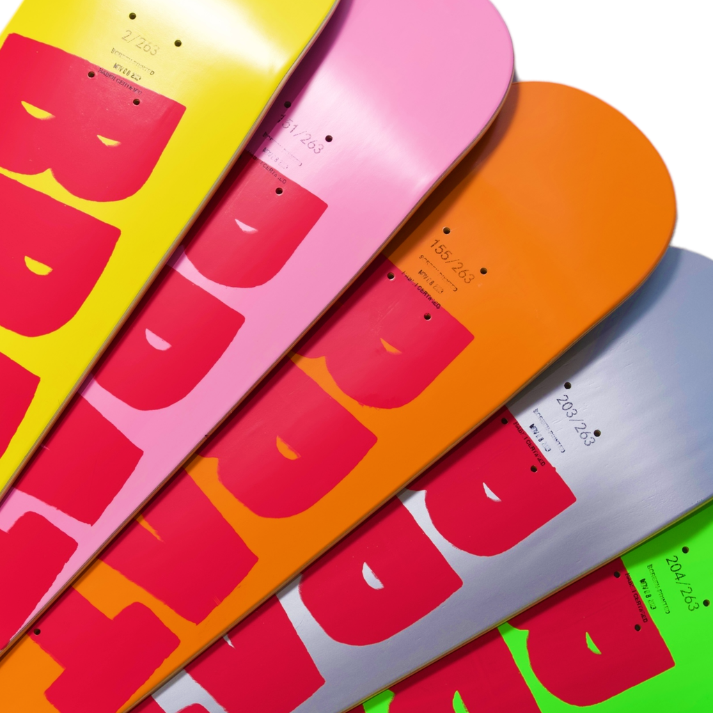 Collection of colorful Carpet Company Brat Logo snowboards with face graphics lined up, varying from pink to orange and grey, each screen printed.