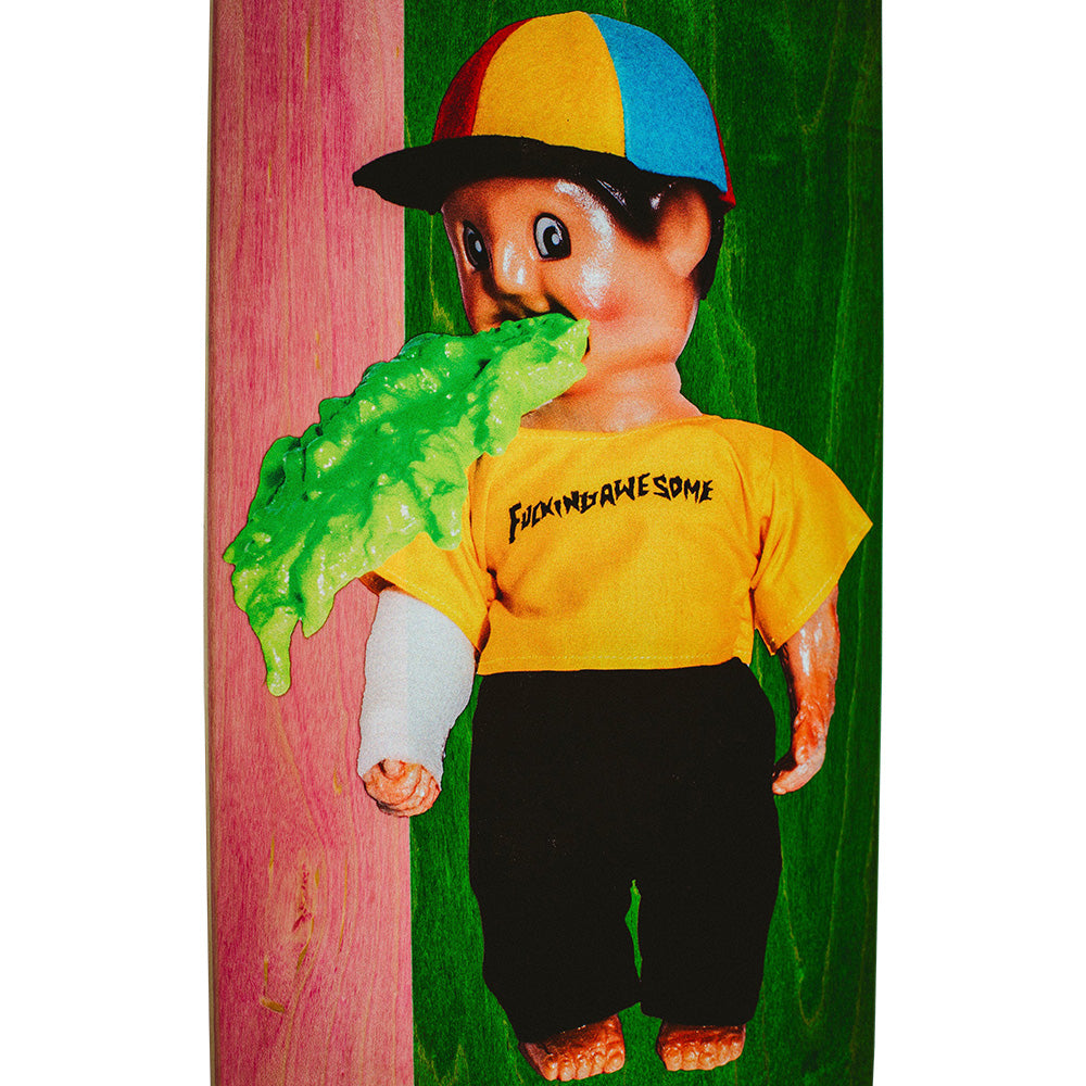 The FUCKING AWESOME WANTO THROW UP MAN doll by FUCKING AWESOME wears a yellow shirt and black pants, features a cast, green slime from its mouth, and comes with an 8.18 x 31.73 skateboard deck at its feet against a colorful background.