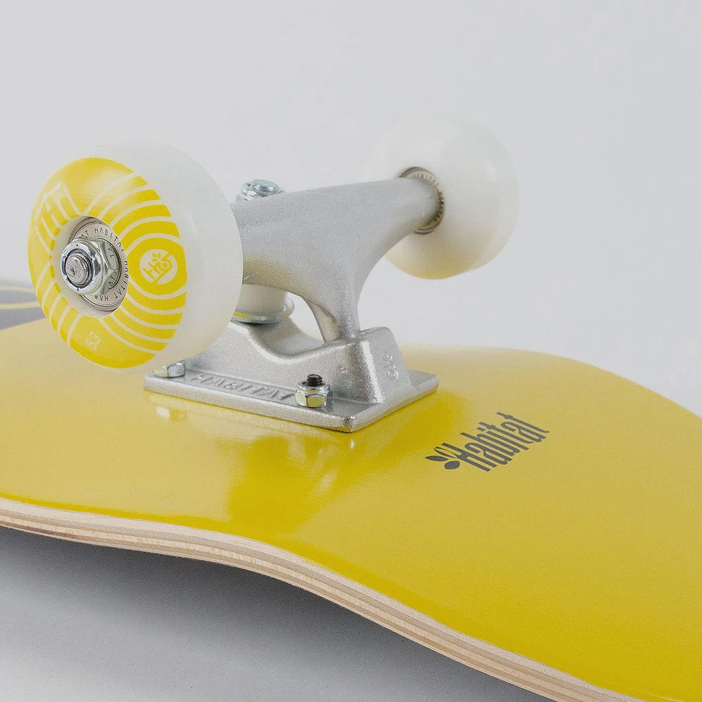 Close-up of a yellow Habitat Pod Complete skateboard with white wheels and silver trucks.