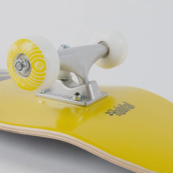 Close-up of a yellow Habitat Pod Complete skateboard with white wheels and silver trucks.