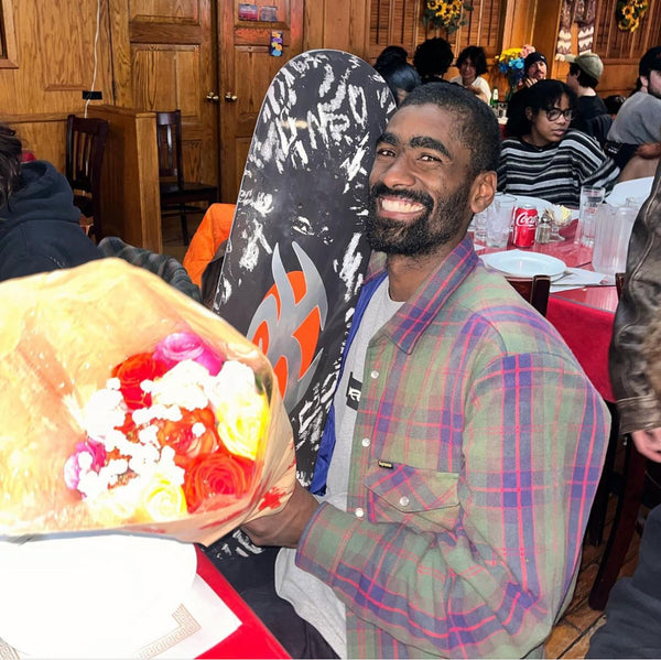 Man sitting at a restaurant table smiling, holding flowers and a LIMOSINE KARIM PRO MODEL SHADOW BOX covered with stickers.