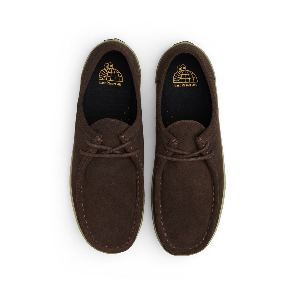 Introducing the LAST RESORT AB VM006 MOC BROWN / GUM from Last Resort AB—a stylish pair of moccasin-style shoes featuring a luxurious brown suede upper, equipped with laces and showcasing an embossed logo on the insole. Enjoy unparalleled comfort with its Cloudy Cush insole.