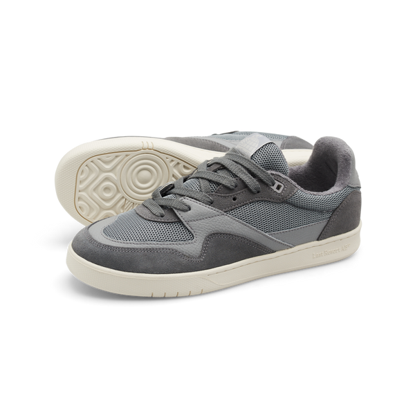 Introducing the LAST RESORT AB CM002 ULTIMATE GREY sneakers by Last Resort AB. These gray shoes feature tactile green mesh panels and white soles, enhanced with suede accents and leather trim. One shoe is seen with its laces tied, while the other leans slightly to the side, capturing a dynamic look.