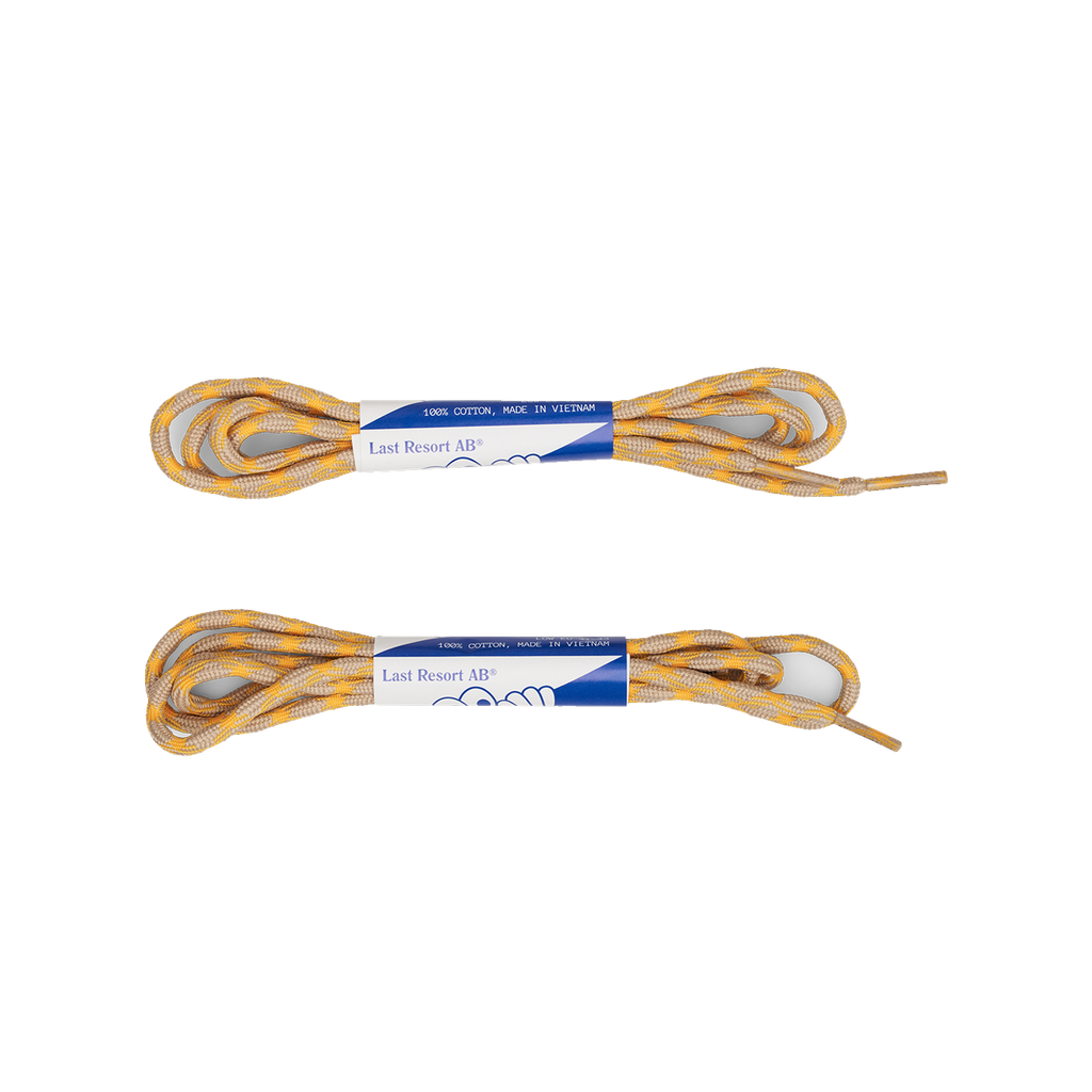 Two pairs of the LAST RESORT AB CM002 TACTILE GREEN shoelaces from Last Resort AB, packaged with blue and white labels, are laid side by side on a pristine white background. Perfect for complementing your favorite suede sneakers or sleek black leather shoes.