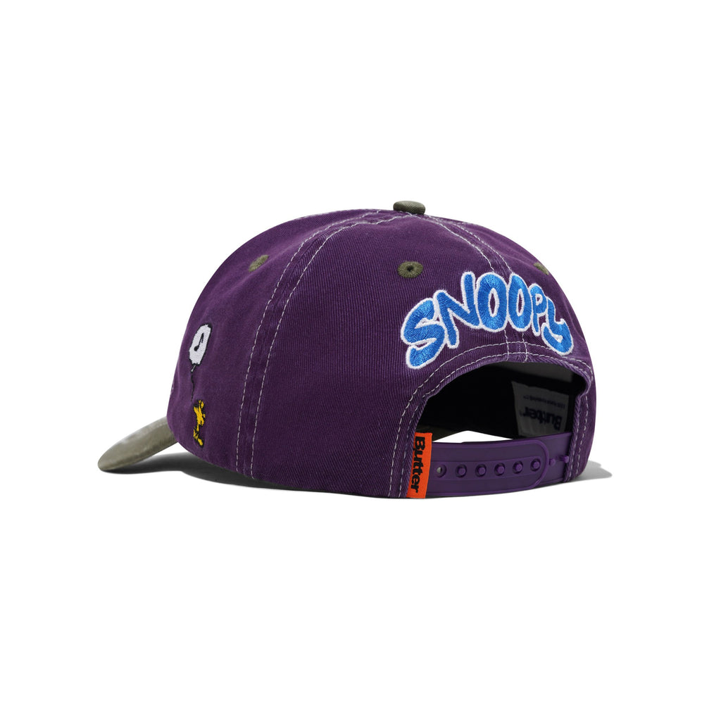 The BUTTER X PEANUTS MUSIC SNAPBACK CAP in washed purple by Butter Goods features "SNOOPY" embroidered in blue and white on the back, an eye graphic on the side, and an adjustable strap for a perfect fit.