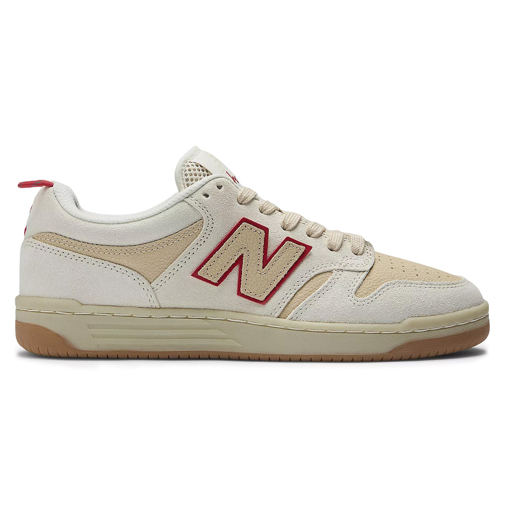 The NB NUMERIC X CHOCOLATE 480 SEA SALT / RED sneaker, from the NB NUMERIC brand, showcases a striking red "N" logo on a beige and white design, complete with a gum sole and reinforced toe cap that harks back to the iconic style of 80s and 90s skate shoes.