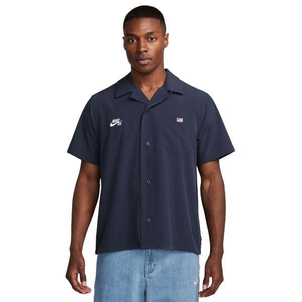 A man wearing the NIKE SB 2024 Federation Kit Button-Up Skate Bowler shirt in Obsidian/White, featuring a small Nike SB logo and an American flag patch, paired with light blue jeans.