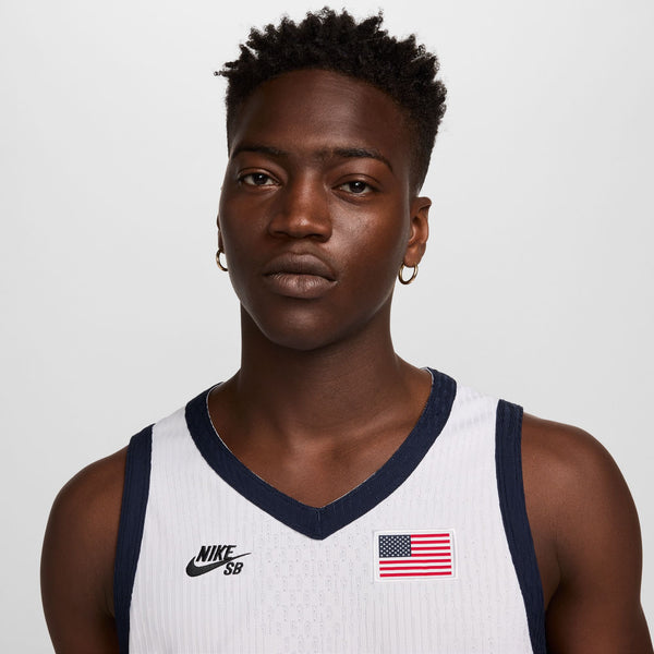 A person with short hair and hoop earrings wears a white NIKE SB 2024 Federation Kit Dri-Fit ADV Sleeveless Skate Jersey USA, showcasing Team USA's spirit.