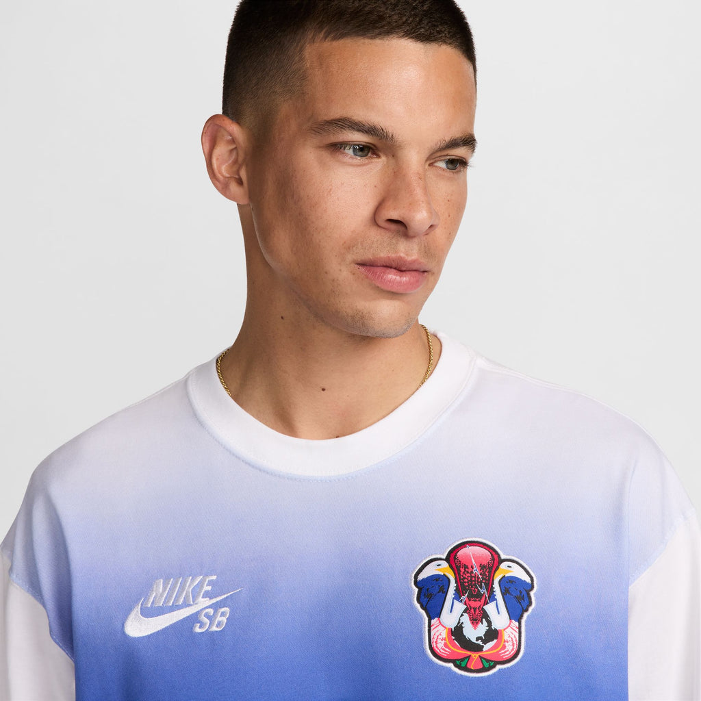 A man with short hair wears a Nike SB 2024 Federation Kit Long Sleeve Skate Tee USA White, featuring a distinctive colorful logo on the left side of the chest.