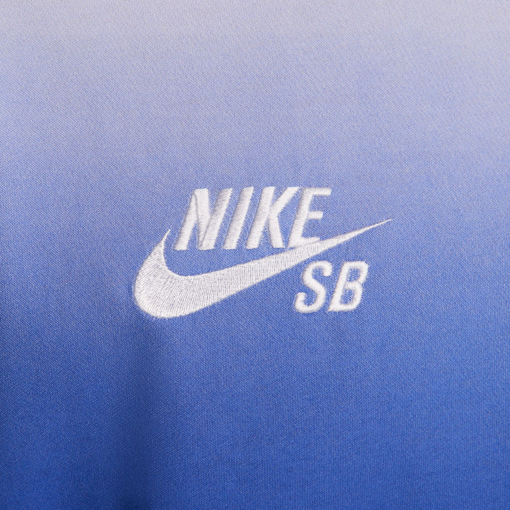 Close-up of a blue gradient fabric featuring the NIKE SB logo in white, from the NIKE SB 2024 Federation Kit Long Sleeve Skate Tee USA White, capturing global inspiration.