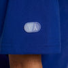 Close-up of the blue fabric from the NIKE SB 2024 Federation Kit Skate Tee USA Old Royal. The small oval patch on it features the letters "Y" and a simplified image of the Eiffel Tower in white, reminiscent of Team USA's pride and athletic passion.