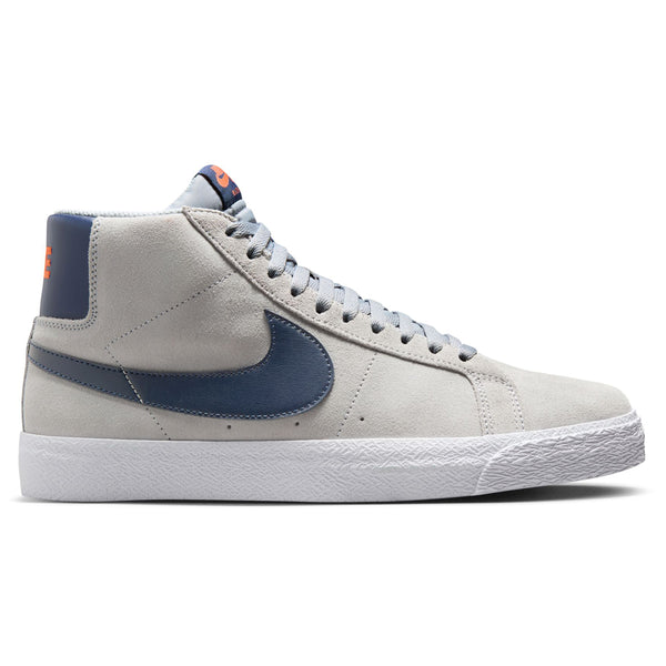 A grey high-top Nike SB Blazer Mid Wolf Grey / Midnight Navy sneaker featuring a blue swoosh, grey laces, and a white textured sole. Orange branding details grace the tongue and heel, while Zoom Air cushioning ensures skateboarders stay comfortable all day.