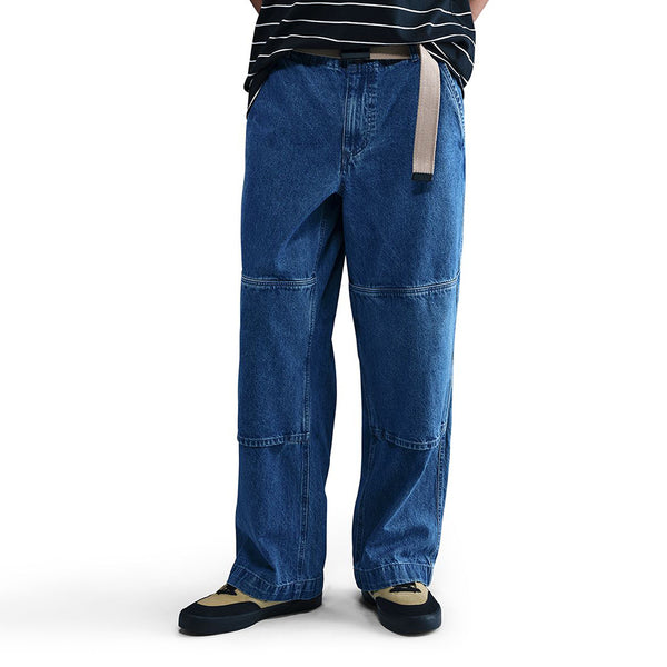 A person wears NIKE SB LOOSE DOUBLE-KNEE DENIM SKATE PANTS by nike, featuring wide legs, durable denim with visible seams, paired with a striped shirt, beige belt, and black and beige shoes. The upper face is not shown; these skate pants blend style and function.