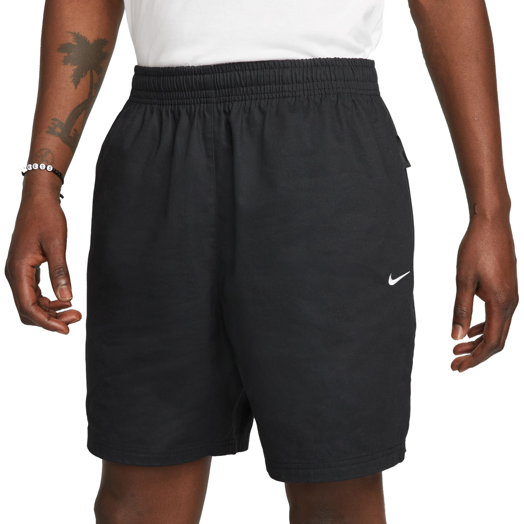 A man in a white shirt and NIKE SB SKYRING SKATE SHORT LOOSE FIT BLACK shorts by Nike.
