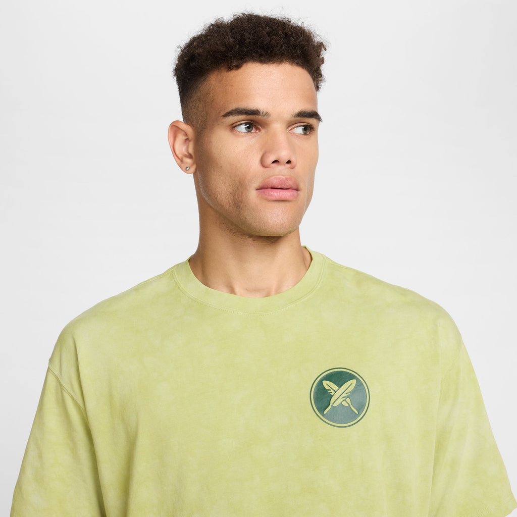 A person in a NIKE SB Yuto Horigome Skate Tee Olive Aura glances to the side against a plain background.