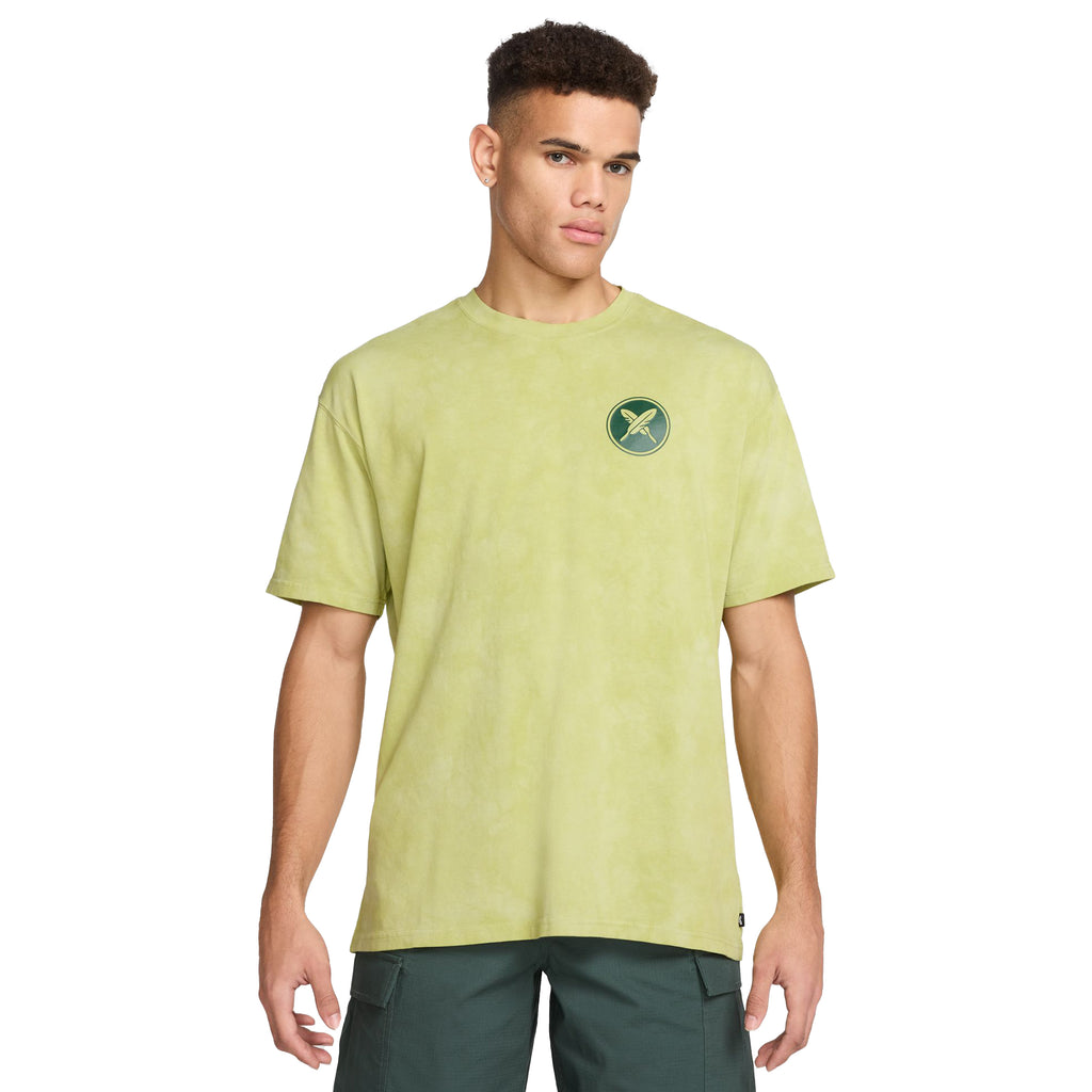 A person wearing a NIKE SB Yuto Horigome Skate Tee in Olive Aura, paired with dark green shorts, standing against a plain white background.