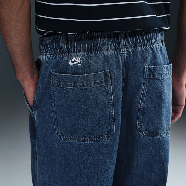 Person wearing nike NIKE SB LOOSE DOUBLE-KNEE DENIM SKATE PANTS, featuring an elastic waistband and two back pockets, shown from behind.