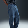 A person wearing NIKE SB LOOSE DOUBLE-KNEE DENIM SKATE PANTS by nike and a black-and-white striped shirt stands against a plain dark background.