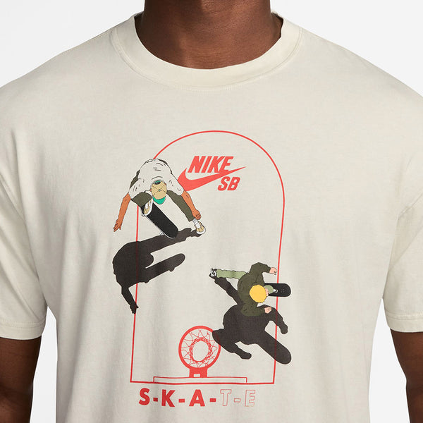 A man wears a beige Nike SB Max90 Court Skate Tee in light bone, made from lightweight cotton, featuring two green and black skateboarders circling a red hoop with "SKATE" at the bottom.