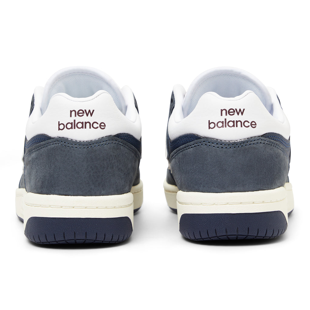 The back view of a blue and white leather shoe with "new balance" written on the heel in marron.
