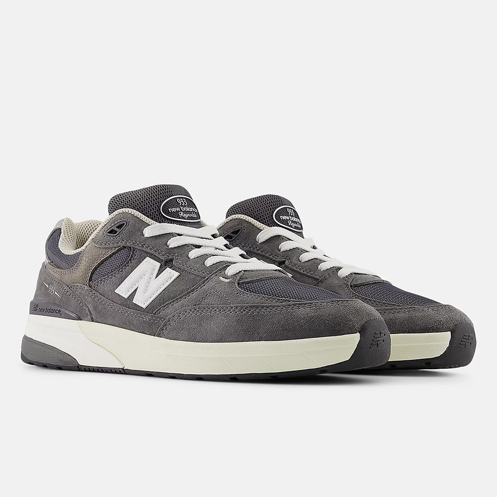 The NB NUMERIC "GREY DAYS" REYNOLDS 933 sneakers in dark grey and white, featuring white laces, heritage design, white midsoles, and the iconic "N" logo on the sides, are displayed against a plain background.