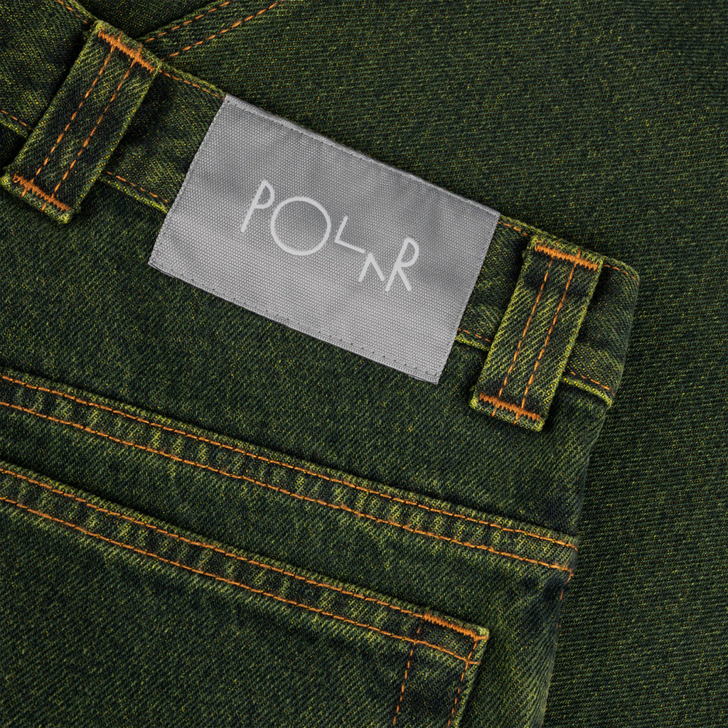 Close-up of an olive-green semi baggy fit denim fabric showing a back pocket and a belt loop with a white rectangular label that reads "POLAR." The stitching around the pocket and label is visible, showcasing the 100% cotton-denim fabric of the POLAR '93! DENIM CHARTREUSE / BLUE by POLAR.