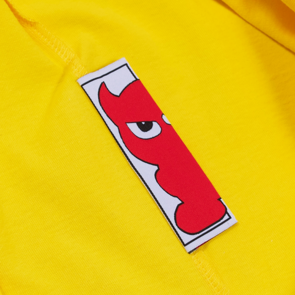 A close up of a Carpet Co. CARPET PEASANT TEE YELLOW with a red devil on it.
