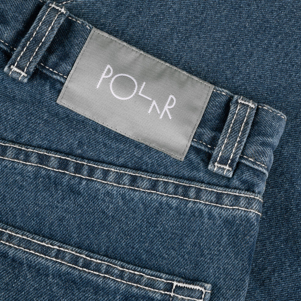 Close-up image of the POLAR '89! DENIM BLUE WASH high-waist denim garment with white stitching and a gray label on the waistband that reads "POLAR.