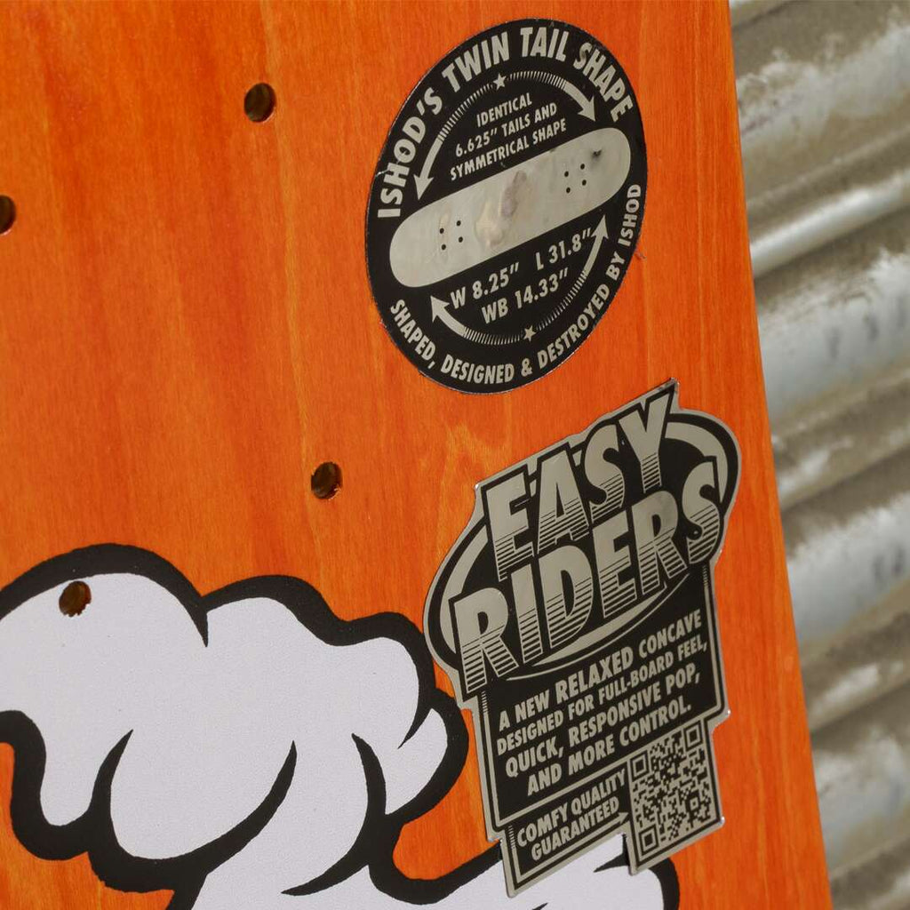 Close-up of the REAL ISHOD MASCOT EASY RIDERS TT skateboard highlighting its "Twin Tail Shape" and relaxed concave, with specifications and design details displayed on the orange deck.