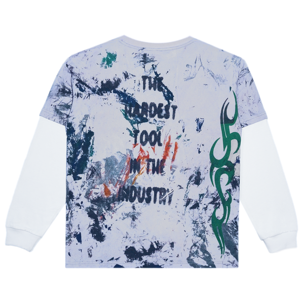 The CARPET RAG TEE LONG SLEEVE by Carpet Co. features a white and blue splattered design with abstract patterns, complemented by a green tribal motif and subtle hints of yellow. The statement "THE HARDEST TOOL IN THE INDUSTRY" adds a vibrant twist reminiscent of a dandelion tee.