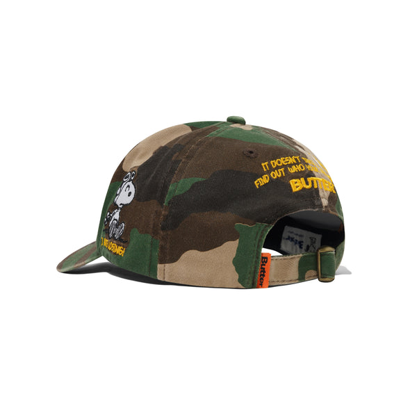 The BUTTER X PEANUTS RATS 6 PANEL CAP WASHED CAMO by Butter Goods is a washed camo cotton twill hat featuring Snoopy embroidered on the side and yellow "It doesn't take much to find out who you are—BUTTER." text on the back.