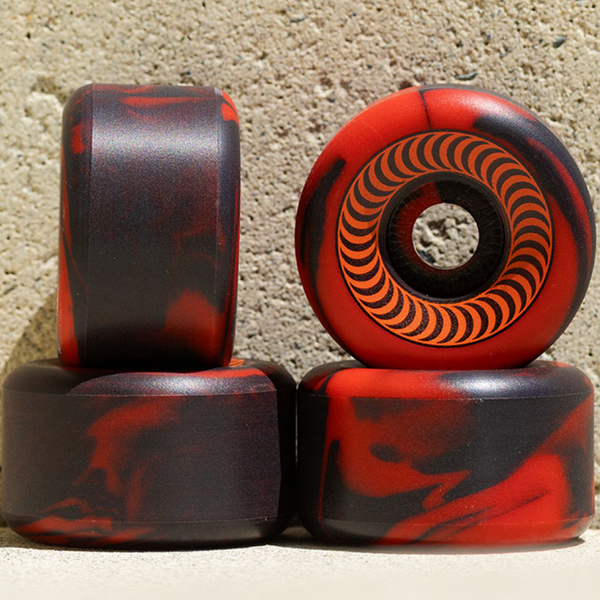 Four SPITFIRE O.G. CLASSICS 99A 54MM RED/BLACK SWIRL skate wheels are stacked against a textured concrete background.