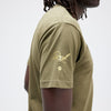 A person wearing a military green STANCE X Ishod Wair Tee, with "Real" and a small logo printed on the sleeve.