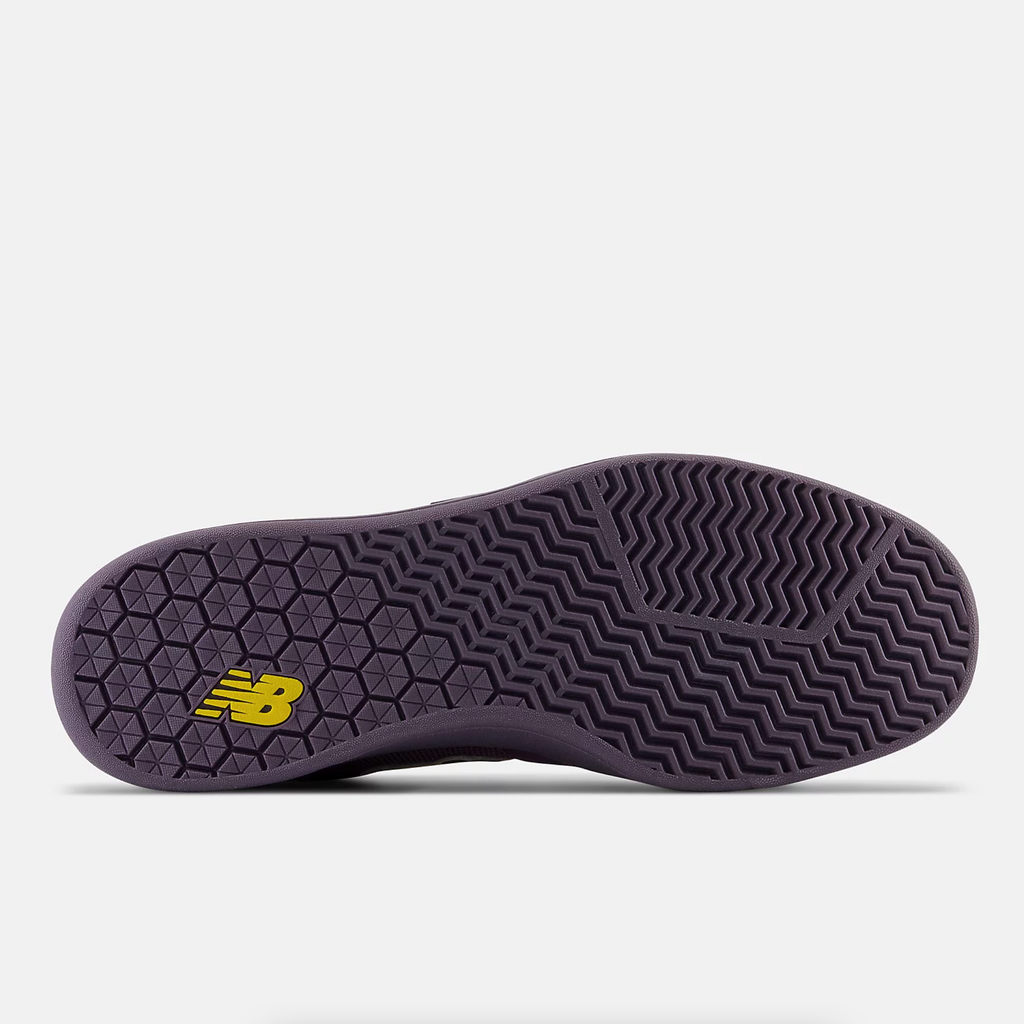 The bottom dark purple sole of a shoe laying down with a yellow NB logo on it.
