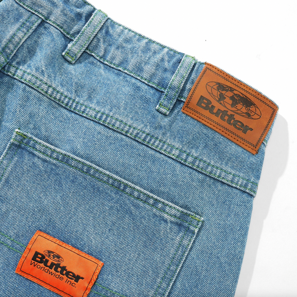 A pair of BUTTER GOODS SANTOSUOSSO DENIM PANT WASHED INDIGO shorts with contrast stitching on the orange label.