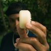 Someone holds a white SPITFIRE F4 ISHOD LOCK-IN CLASSICS 99D 52MM skateboard wheel close to the camera, with blurred greenery in the background.