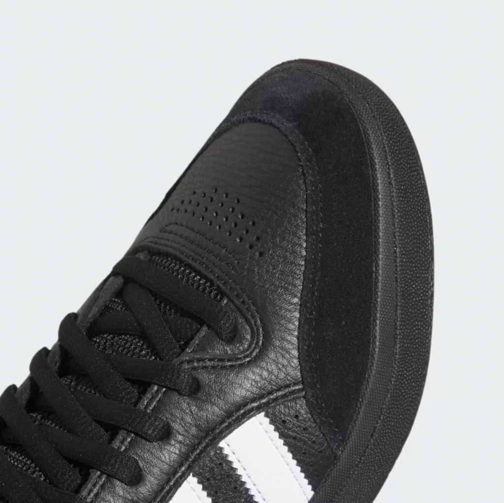 A close-up of the ADIDAS Tyshawn Low sneaker in Core Black with a textured leather and suede upper, showcasing three Cloud White stripes on the side and enhanced comfort from its memory foam collar.