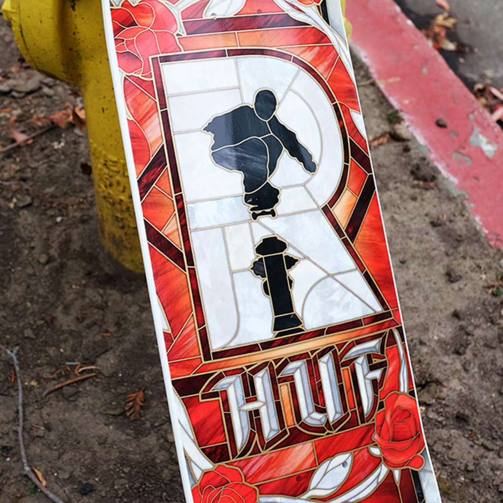 The REAL HUF CATHEDRAL skateboard deck by REAL is 8.28" wide, featuring a stained glass-style design with a skateboarder, fire hydrant, red roses, and "HUF" at the bottom—part of the MASON VICIOUSOG construction collection.