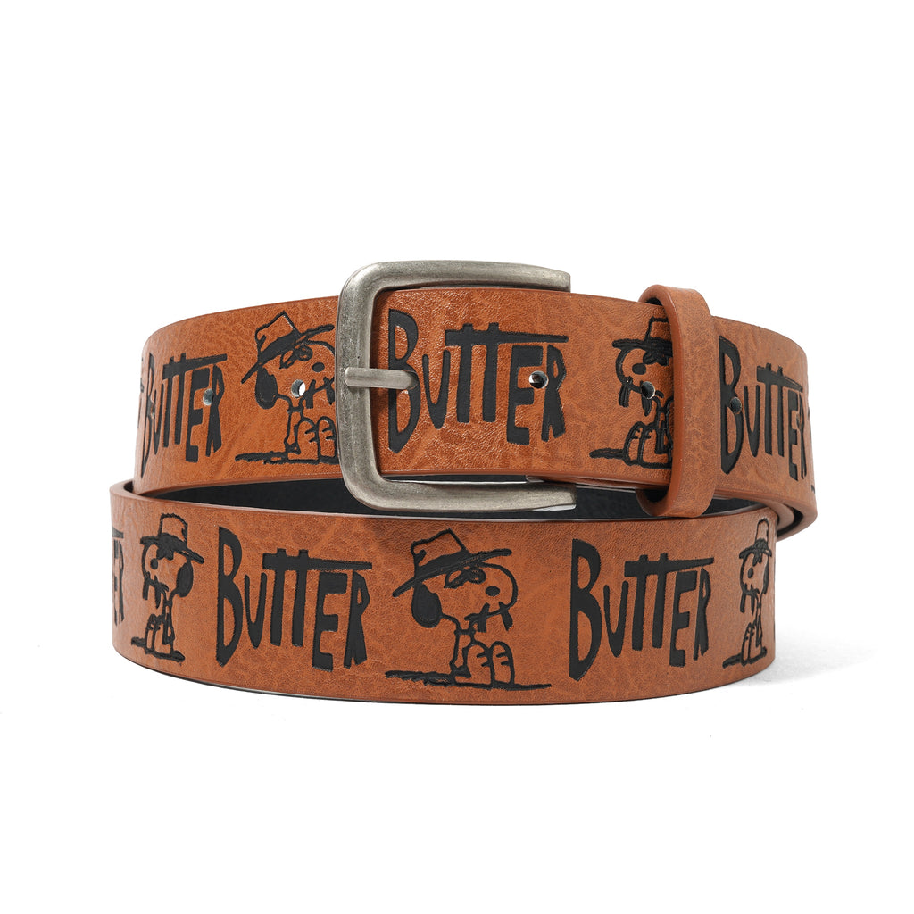 The BUTTER X PEANUTS SPIKE BELT BROWN by Butter Goods is a brown PU leather belt with embossed patterns, Snoopy in a hat, bold black "BUTTER" text, and a silver buckle.