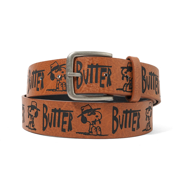 The BUTTER X PEANUTS SPIKE BELT BROWN by Butter Goods is a brown PU leather belt with embossed patterns, Snoopy in a hat, bold black "BUTTER" text, and a silver buckle.