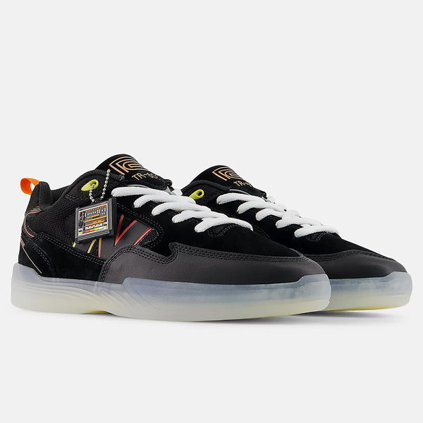 The NB Numeric Tiago x Roland 808 Lite Black/Orange sneakers feature translucent soles, orange accents, and a branded hang tag, displayed against a plain background.