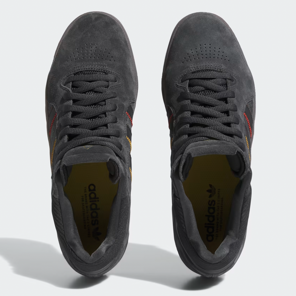 A pair of ADIDAS TYSHAWN CARBON / CORE BLACK / PRELOVED BROWN men's grey shoes with a red and yellow stripe.