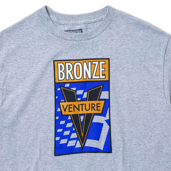 Heather grey tee from VENTURE featuring a bold graphic design of a large "V" with the text "Bronze Venture" set against a blue and orange backdrop with abstract shapes, capturing the dynamic spirit of Venture X.