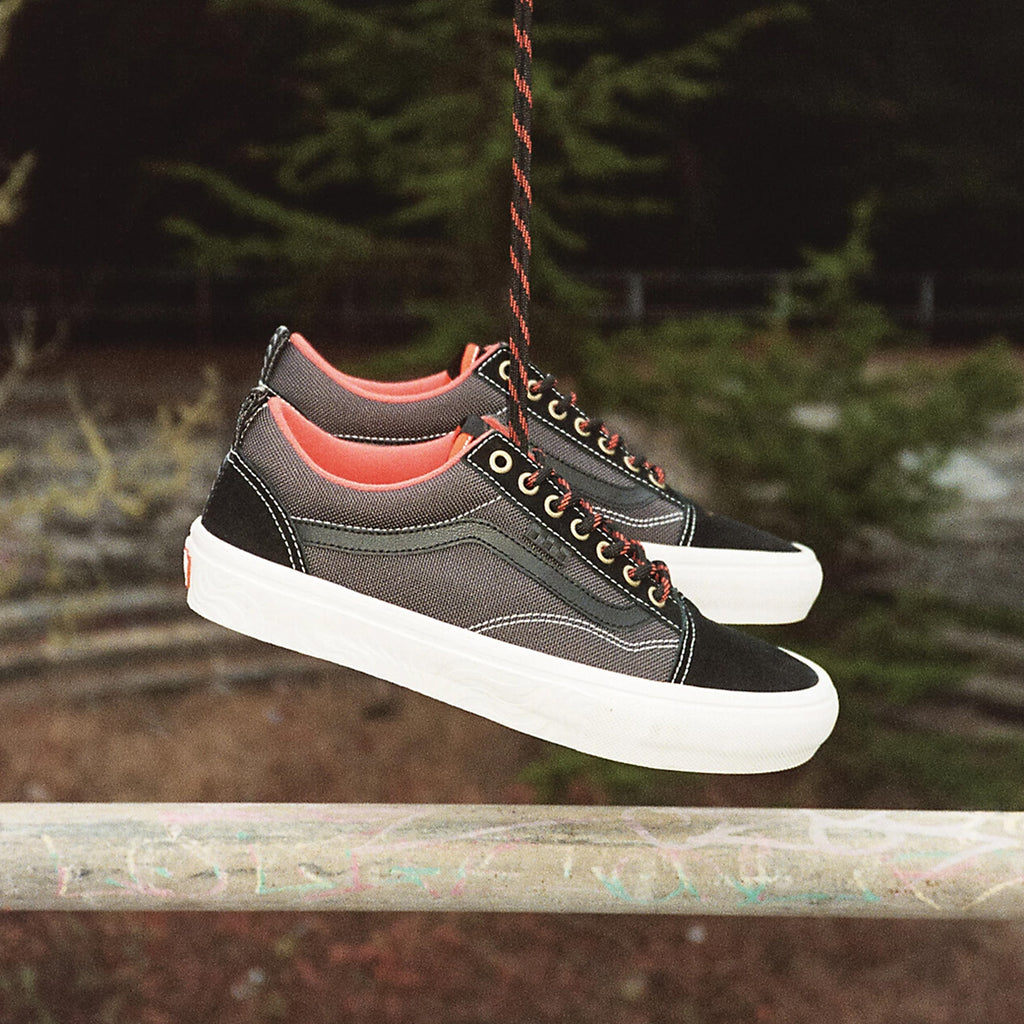 A pair of Vans X Spitfire Skate Old Skool Black/Flame sneakers from the Skate Classics collection hanging from a railing, showcasing their increased durability.